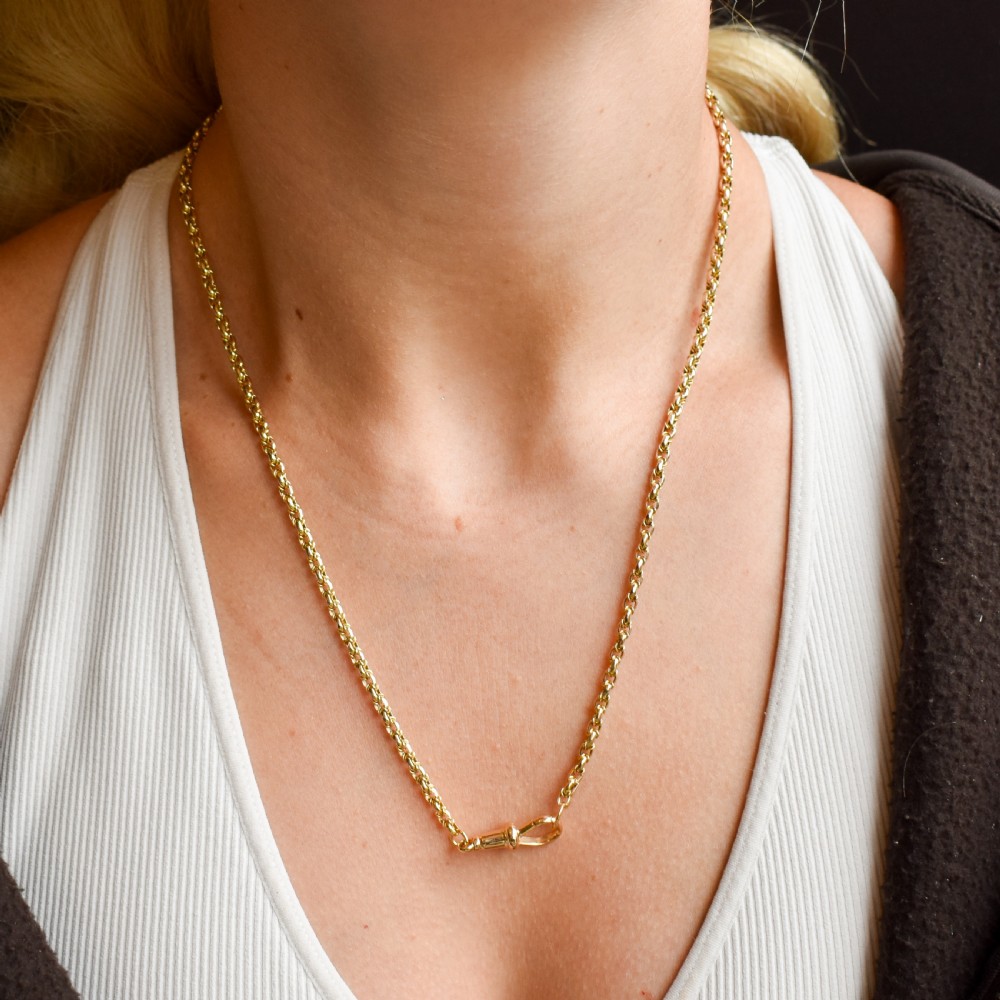 An antique 9ct yellow gold fancy link chain necklace with a dog clip clasp displayed on a green surface. View VII