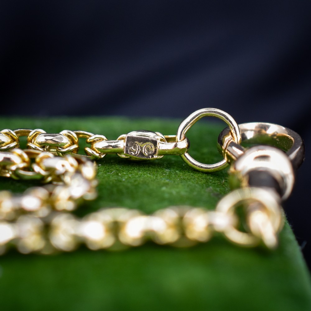 An antique 9ct yellow gold fancy link chain necklace with a dog clip clasp displayed on a green surface. View X
