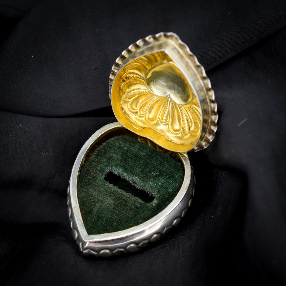 An open heart-shaped sterling silver ring box featuring an embossed gilt interior lid and a green velvet base slot for a ring.