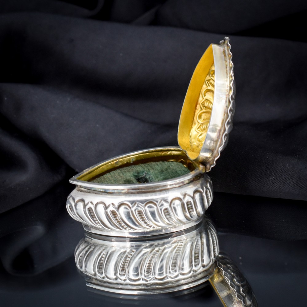 An open heart-shaped sterling silver ring box featuring an embossed gilt interior lid and a green velvet base slot for a ring. View V