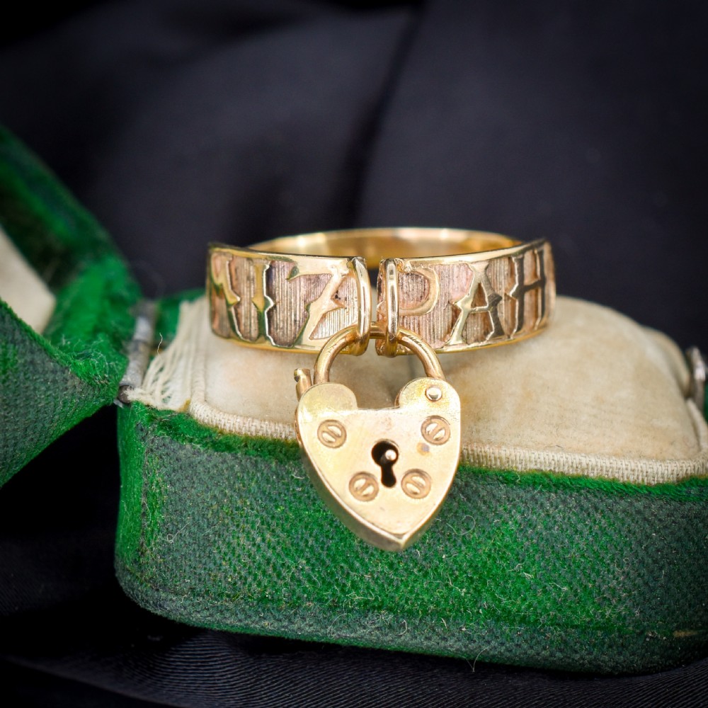 A vintage 9ct yellow gold band ring featuring relief MIZPAH lettering and a dangling heart padlock charm. View VI