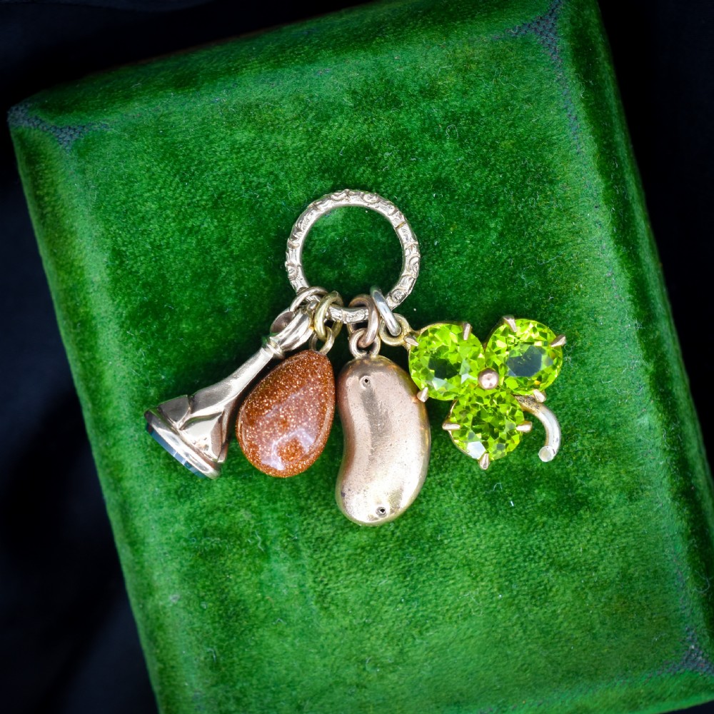An antique gold engraved split ring holding four charms, including a green peridot shamrock, a gold bean, a tear-shaped goldstone, and a gold seal fob.