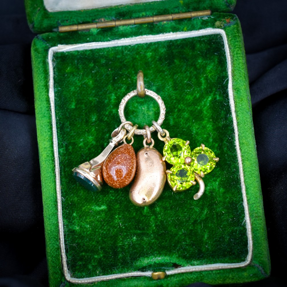 An antique gold engraved split ring holding four charms, including a green peridot shamrock, a gold bean, a tear-shaped goldstone, and a gold seal fob. View II