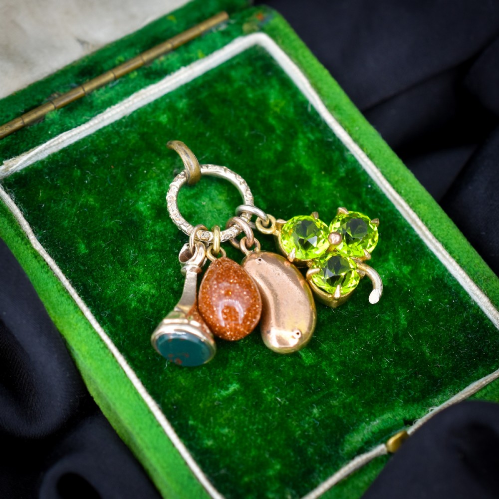 An antique gold engraved split ring holding four charms, including a green peridot shamrock, a gold bean, a tear-shaped goldstone, and a gold seal fob. View III