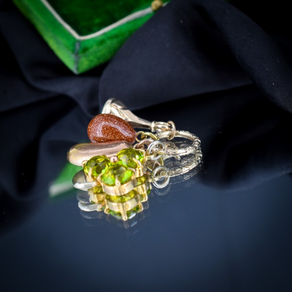 An antique gold engraved split ring holding four charms, including a green peridot shamrock, a gold bean, a tear-shaped goldstone, and a gold seal fob. View IV
