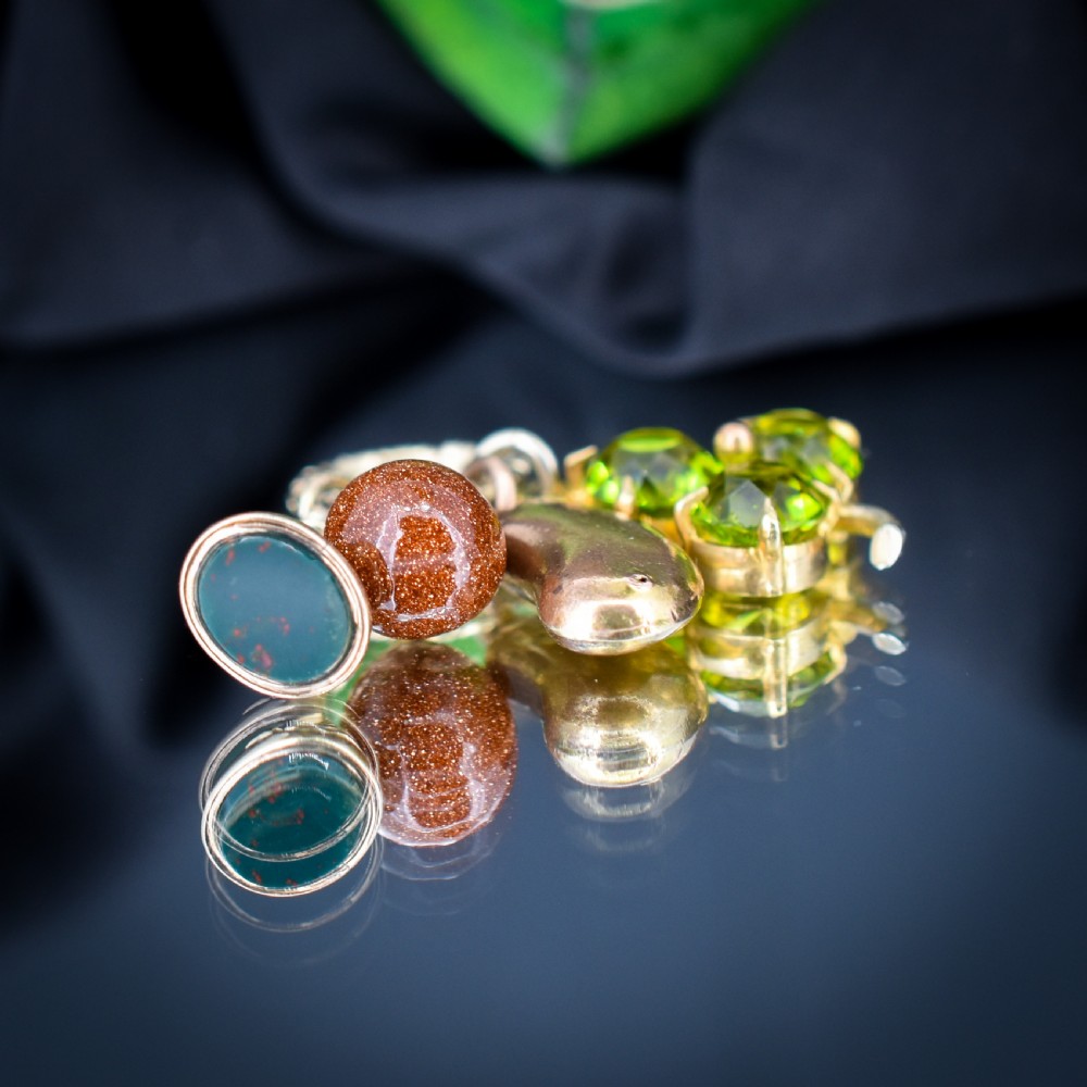 An antique gold engraved split ring holding four charms, including a green peridot shamrock, a gold bean, a tear-shaped goldstone, and a gold seal fob. View V