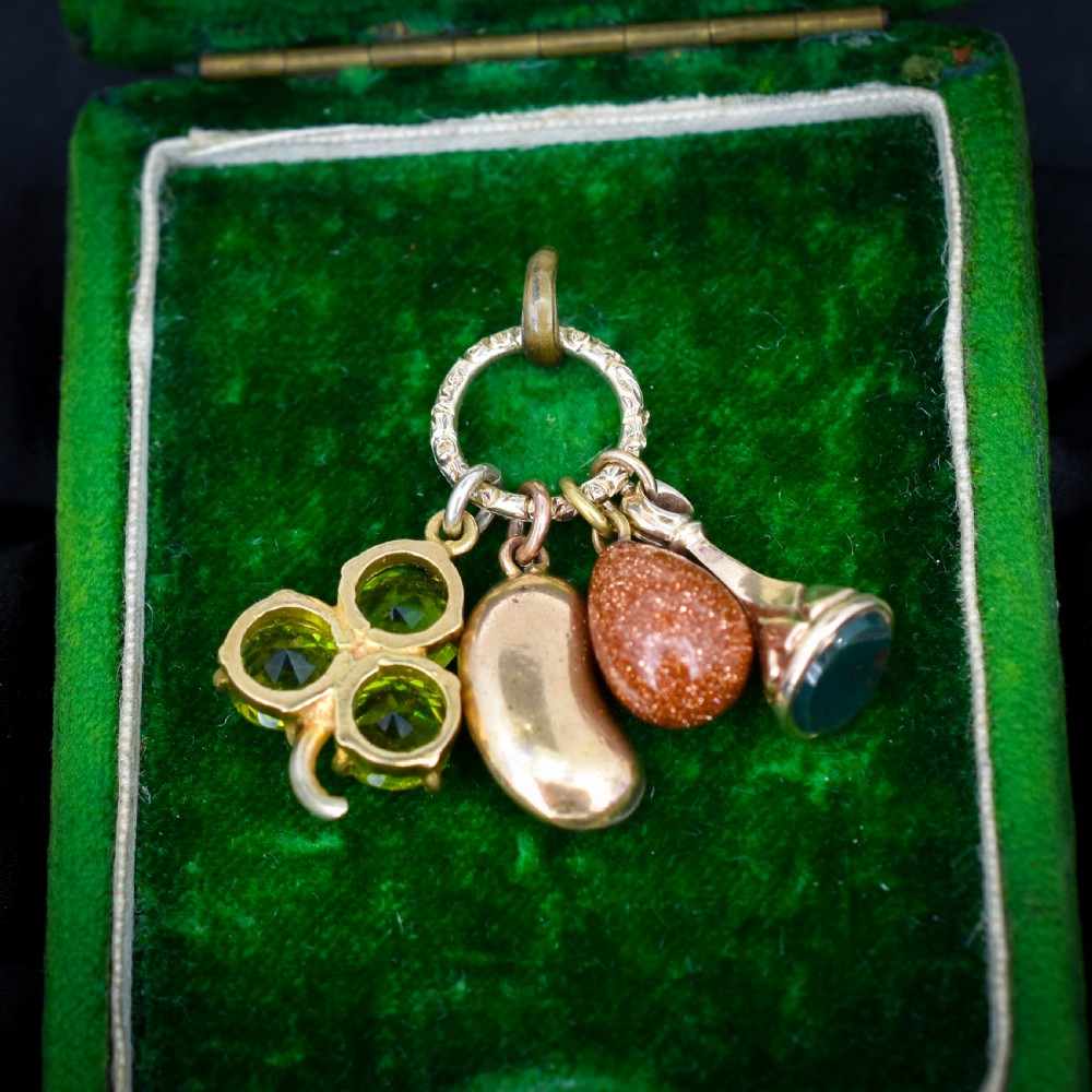 An antique gold engraved split ring holding four charms, including a green peridot shamrock, a gold bean, a tear-shaped goldstone, and a gold seal fob. View VI