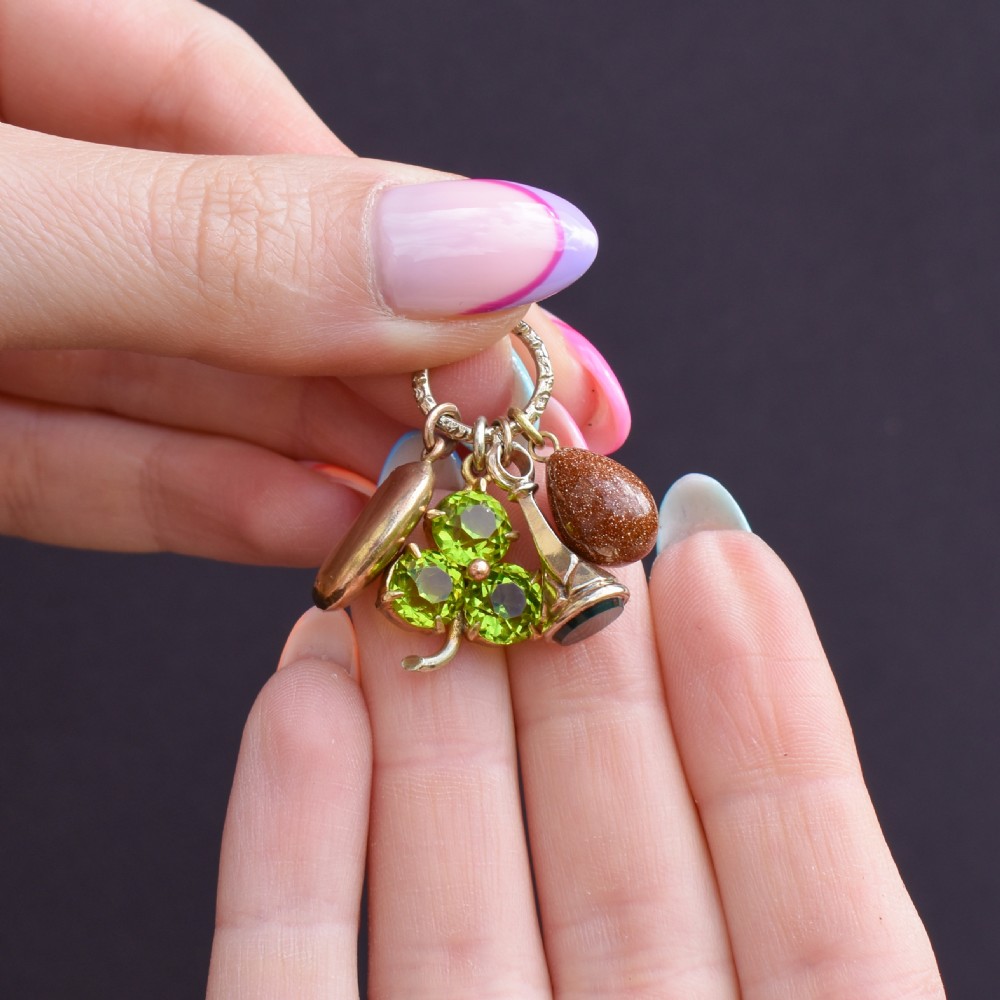 An antique gold engraved split ring holding four charms, including a green peridot shamrock, a gold bean, a tear-shaped goldstone, and a gold seal fob. View VII