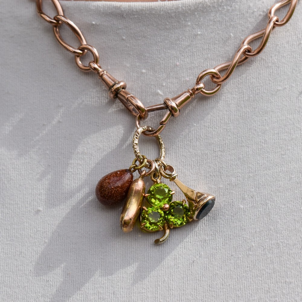 An antique gold engraved split ring holding four charms, including a green peridot shamrock, a gold bean, a tear-shaped goldstone, and a gold seal fob. View IX