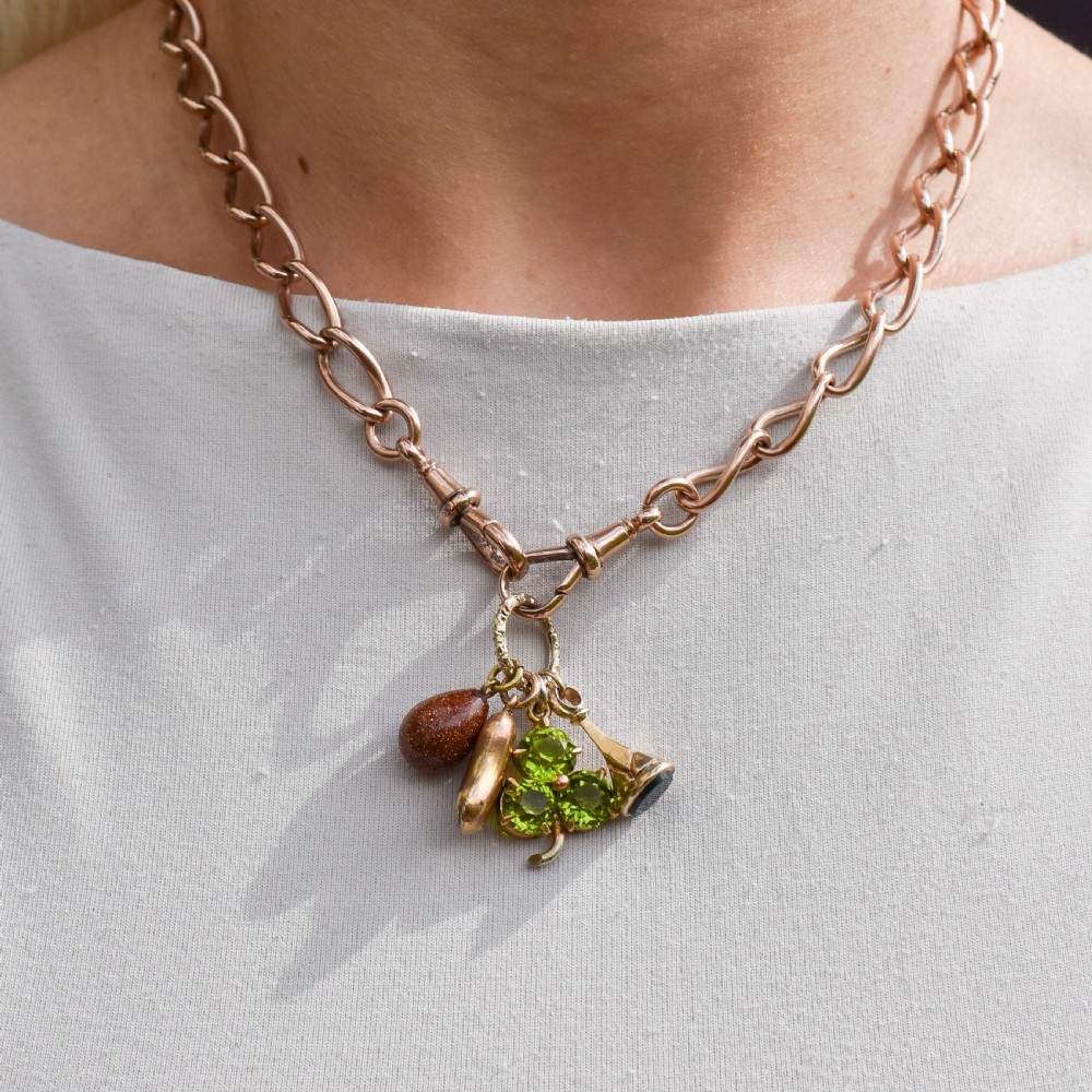 An antique gold engraved split ring holding four charms, including a green peridot shamrock, a gold bean, a tear-shaped goldstone, and a gold seal fob. View X