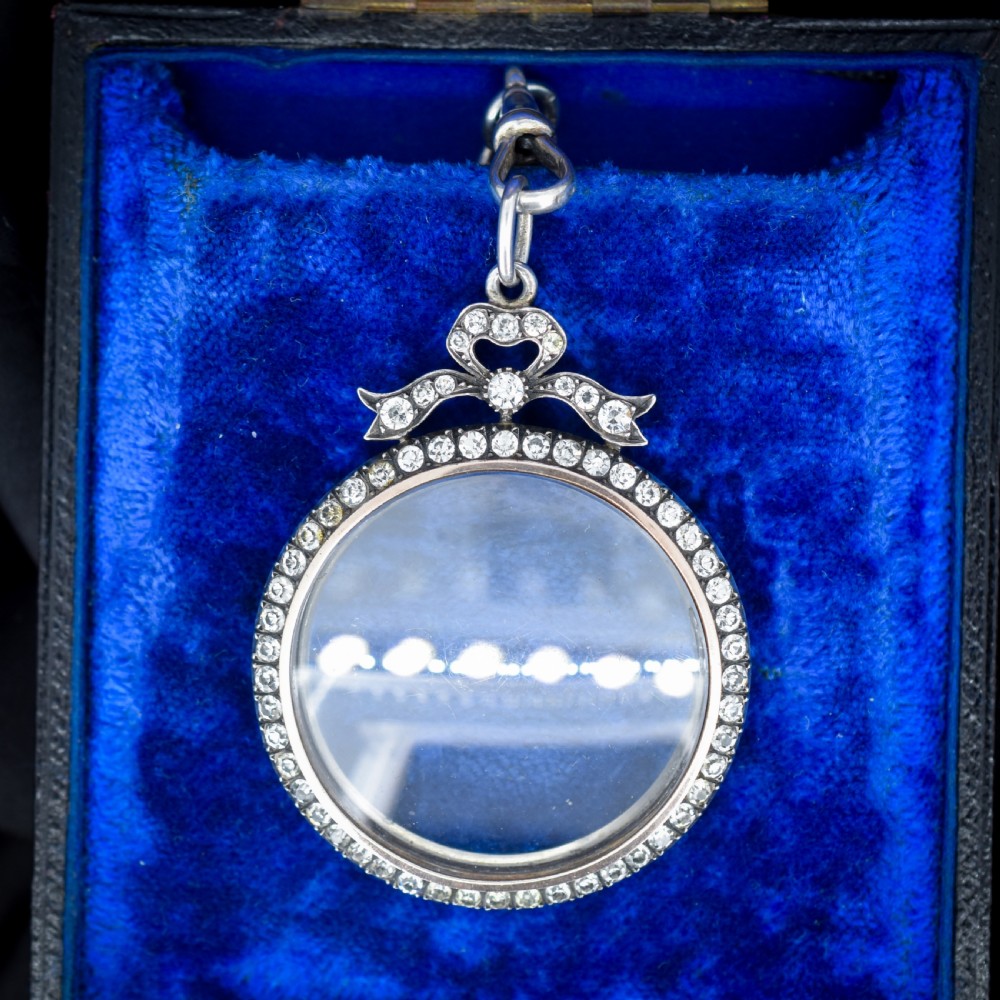 An Edwardian circular silver pendant featuring a clear glass shaker compartment framed by paste stones and topped with a decorative ribbon bow. View II