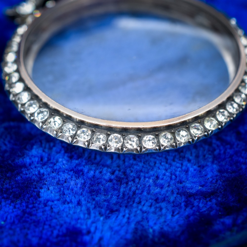 An Edwardian circular silver pendant featuring a clear glass shaker compartment framed by paste stones and topped with a decorative ribbon bow. View III