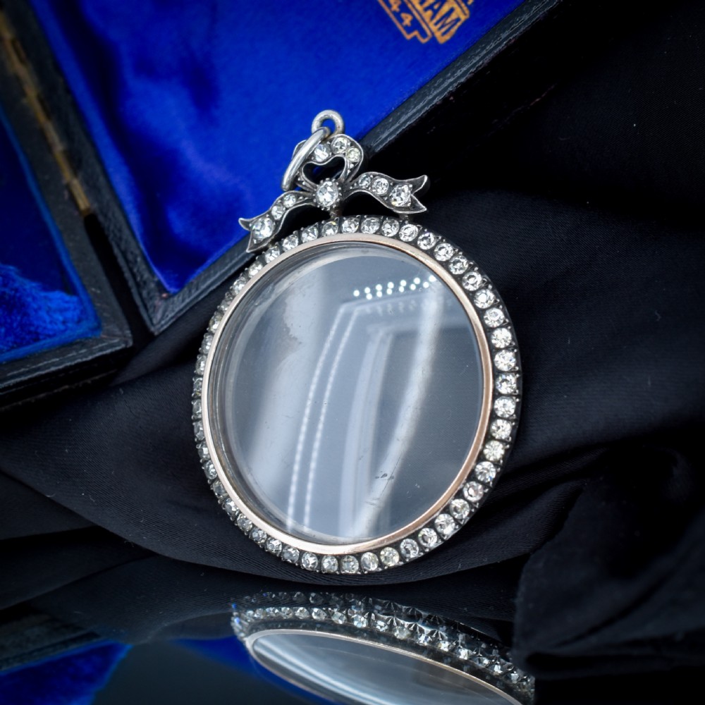 An Edwardian circular silver pendant featuring a clear glass shaker compartment framed by paste stones and topped with a decorative ribbon bow. View IV