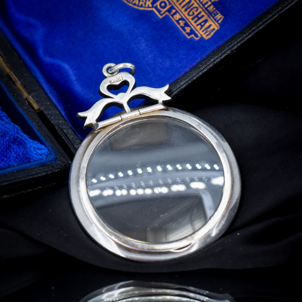 An Edwardian circular silver pendant featuring a clear glass shaker compartment framed by paste stones and topped with a decorative ribbon bow. View VI