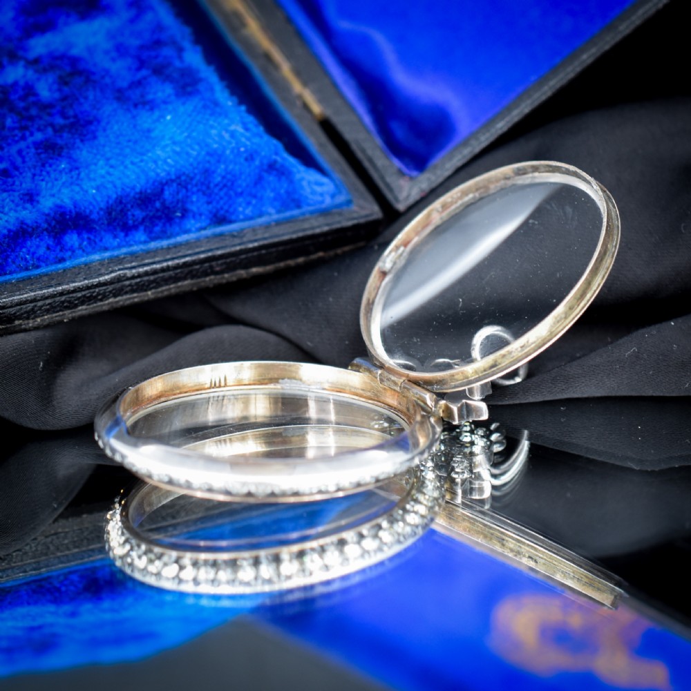 An Edwardian circular silver pendant featuring a clear glass shaker compartment framed by paste stones and topped with a decorative ribbon bow. View VII