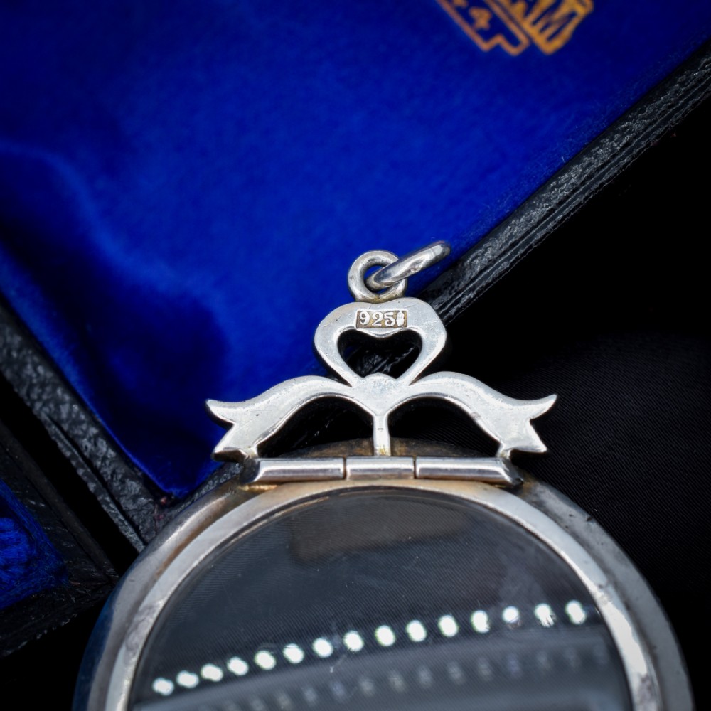 An Edwardian circular silver pendant featuring a clear glass shaker compartment framed by paste stones and topped with a decorative ribbon bow. View VIII
