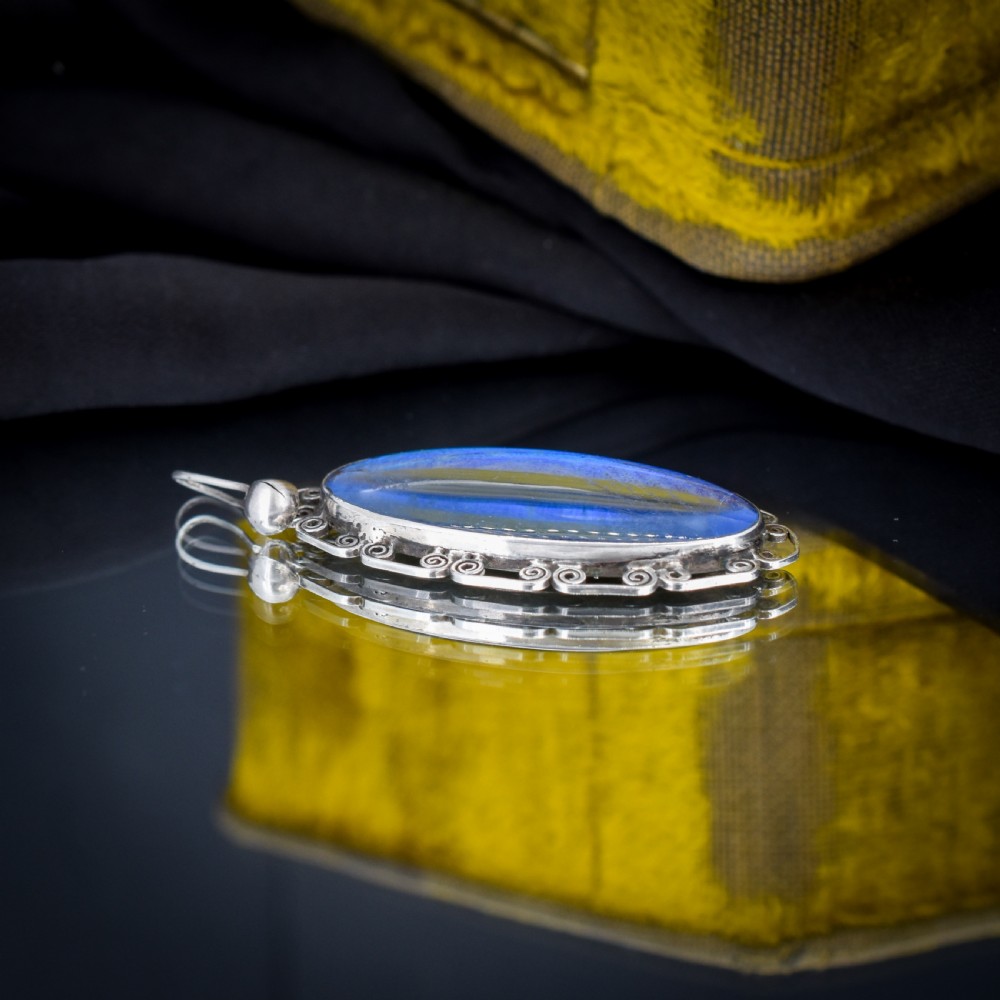 An elongated oval sterling silver Art Deco pendant enclosing a vivid blue butterfly wing with a scrolled wirework outer frame. View III