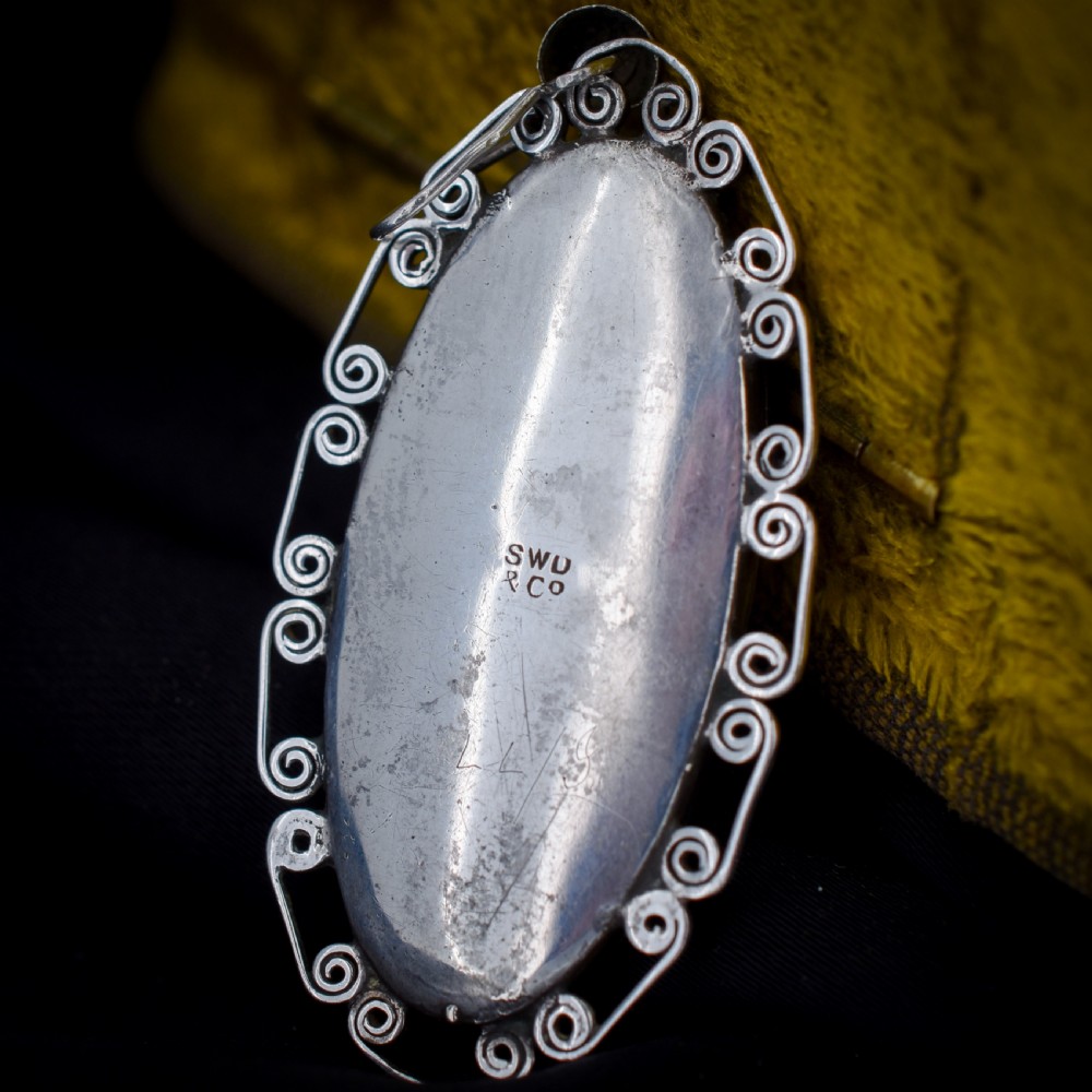 An elongated oval sterling silver Art Deco pendant enclosing a vivid blue butterfly wing with a scrolled wirework outer frame. View VI