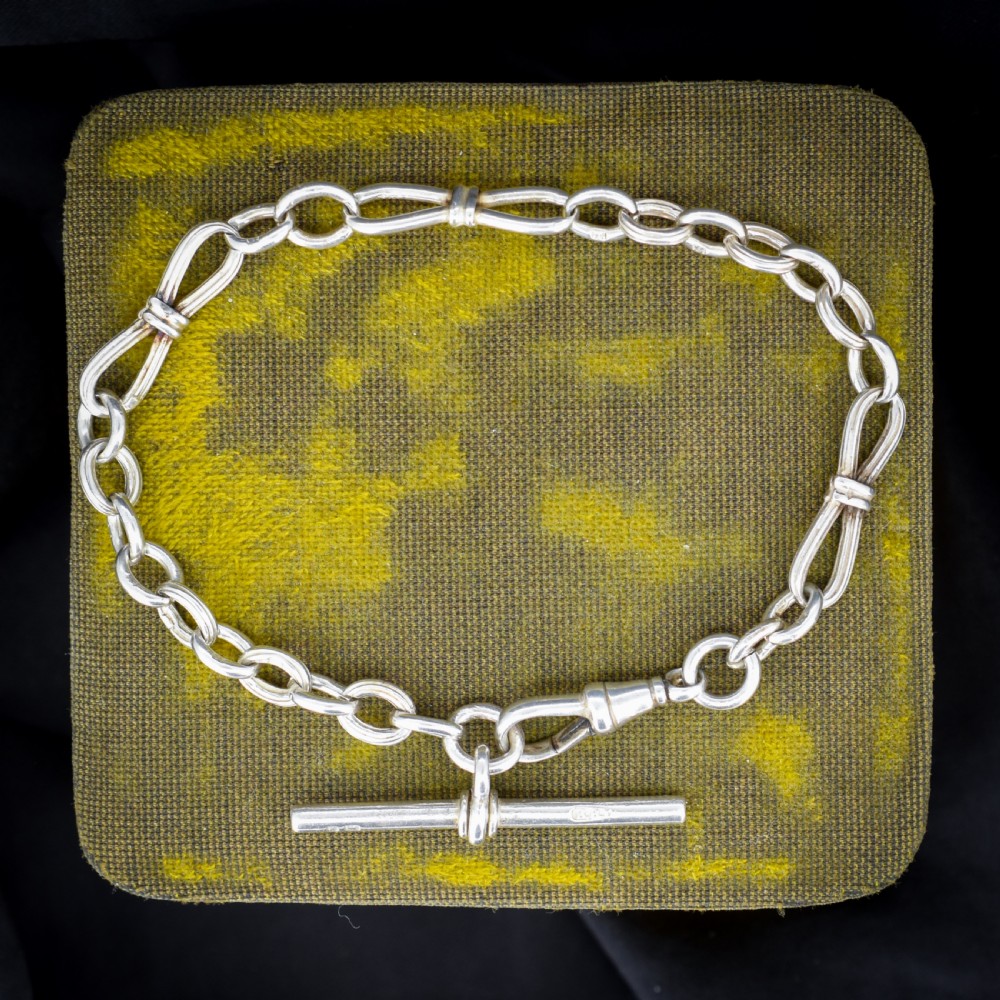 An antique sterling silver fancy link chain bracelet featuring a dog clip fastener and a suspended T-bar drop.