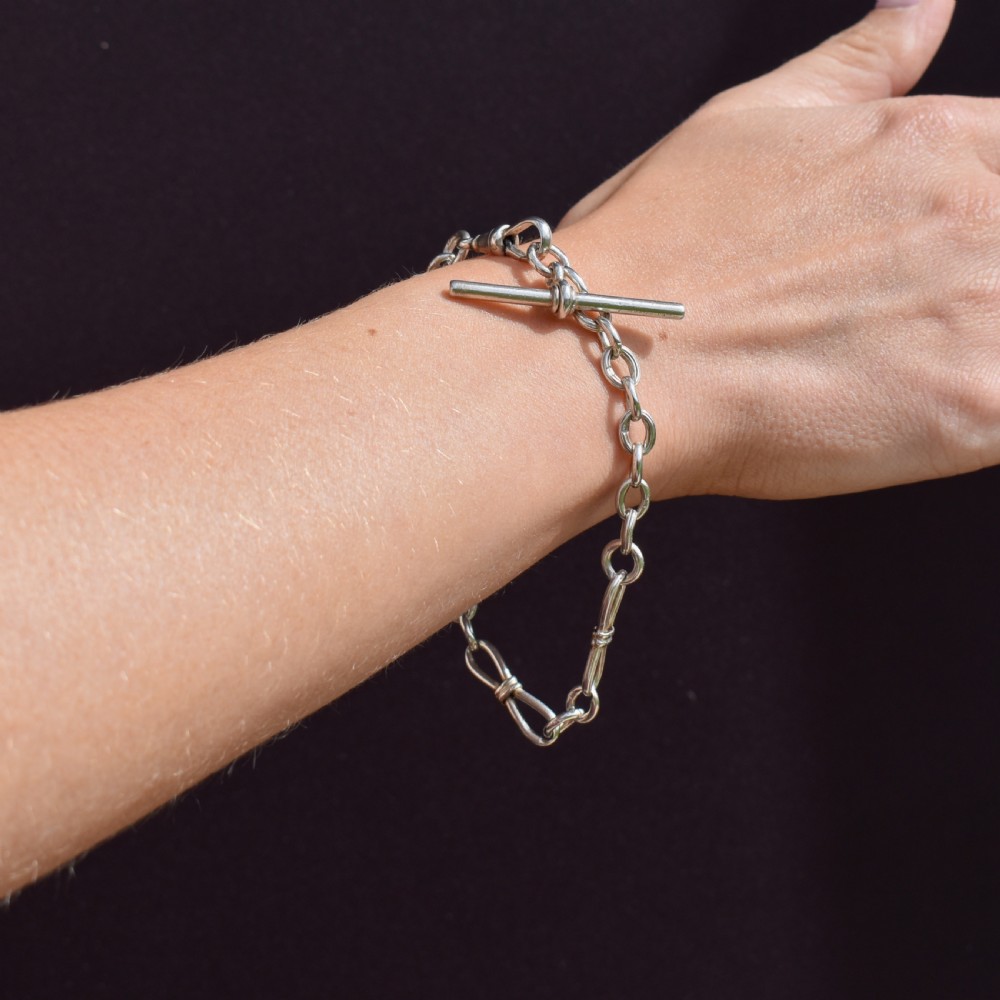 An antique sterling silver fancy link chain bracelet featuring a dog clip fastener and a suspended T-bar drop. View X