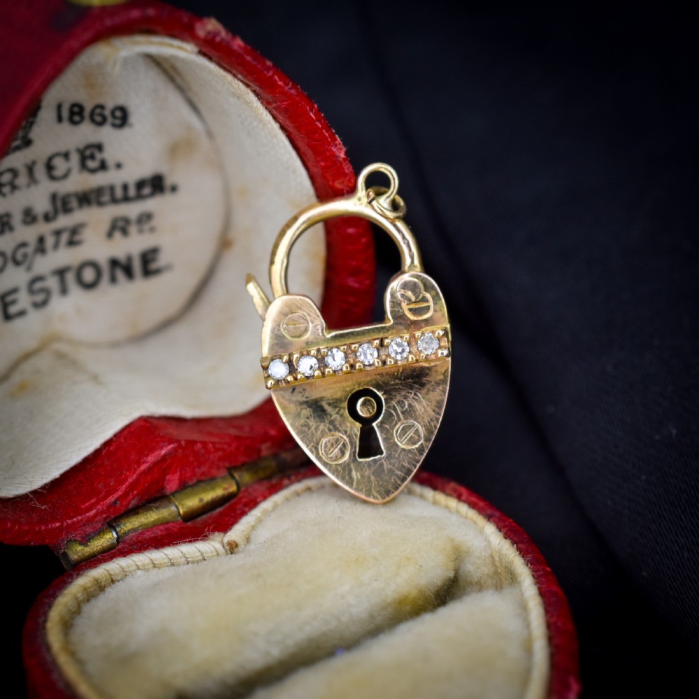 An antique 9ct yellow gold heart-shaped padlock charm set with a row of small round diamonds across the centre bar and featuring an engraved keyhole design.