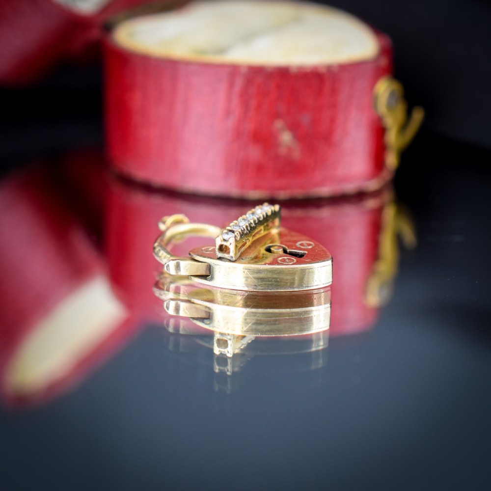 An antique 9ct yellow gold heart-shaped padlock charm set with a row of small round diamonds across the centre bar and featuring an engraved keyhole design. View VII
