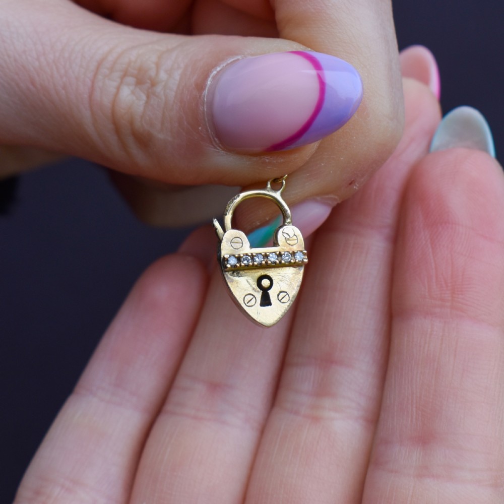 An antique 9ct yellow gold heart-shaped padlock charm set with a row of small round diamonds across the centre bar and featuring an engraved keyhole design. View VIII