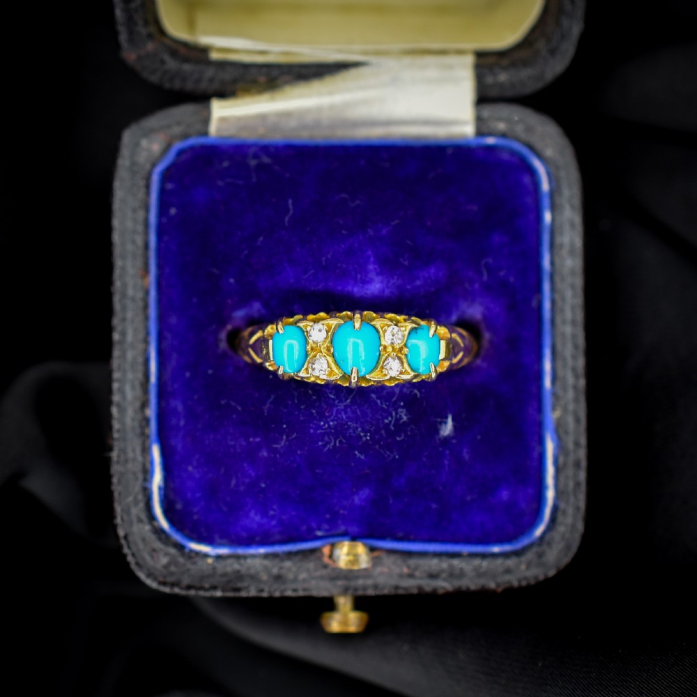 An antique 18ct yellow gold Edwardian boat ring set with three oval turquoise cabochons and four accent diamonds, featuring carved scrollwork along the gallery.