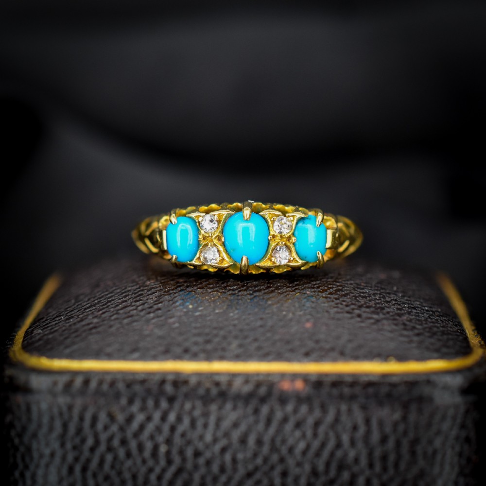 An antique 18ct yellow gold Edwardian boat ring set with three oval turquoise cabochons and four accent diamonds, featuring carved scrollwork along the gallery. View II