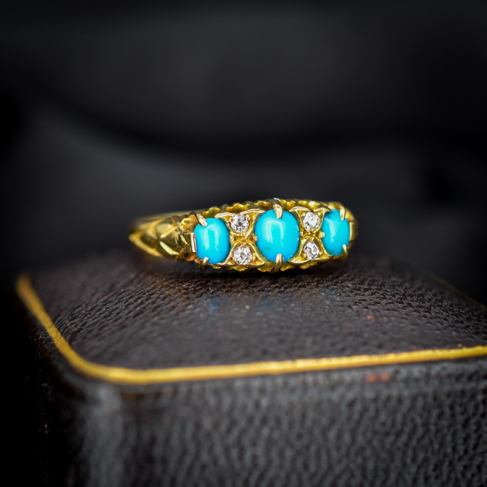 An antique 18ct yellow gold Edwardian boat ring set with three oval turquoise cabochons and four accent diamonds, featuring carved scrollwork along the gallery. View III