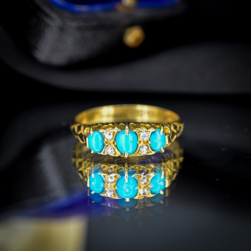 An antique 18ct yellow gold Edwardian boat ring set with three oval turquoise cabochons and four accent diamonds, featuring carved scrollwork along the gallery. View IV
