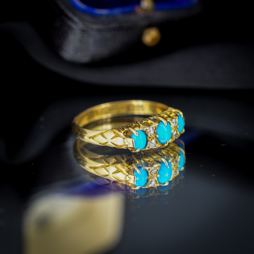 An antique 18ct yellow gold Edwardian boat ring set with three oval turquoise cabochons and four accent diamonds, featuring carved scrollwork along the gallery. View V