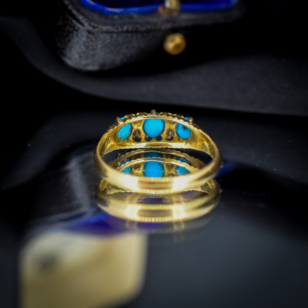 An antique 18ct yellow gold Edwardian boat ring set with three oval turquoise cabochons and four accent diamonds, featuring carved scrollwork along the gallery. View VI