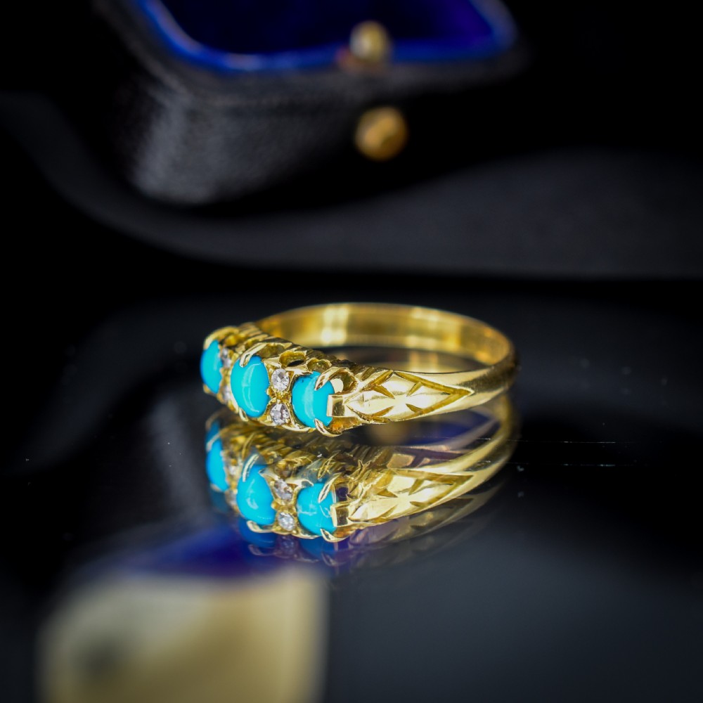 An antique 18ct yellow gold Edwardian boat ring set with three oval turquoise cabochons and four accent diamonds, featuring carved scrollwork along the gallery. View VII