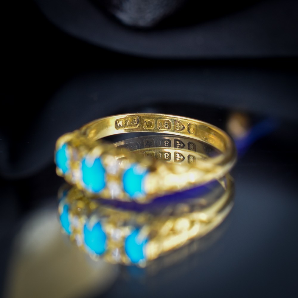 An antique 18ct yellow gold Edwardian boat ring set with three oval turquoise cabochons and four accent diamonds, featuring carved scrollwork along the gallery. View VIII