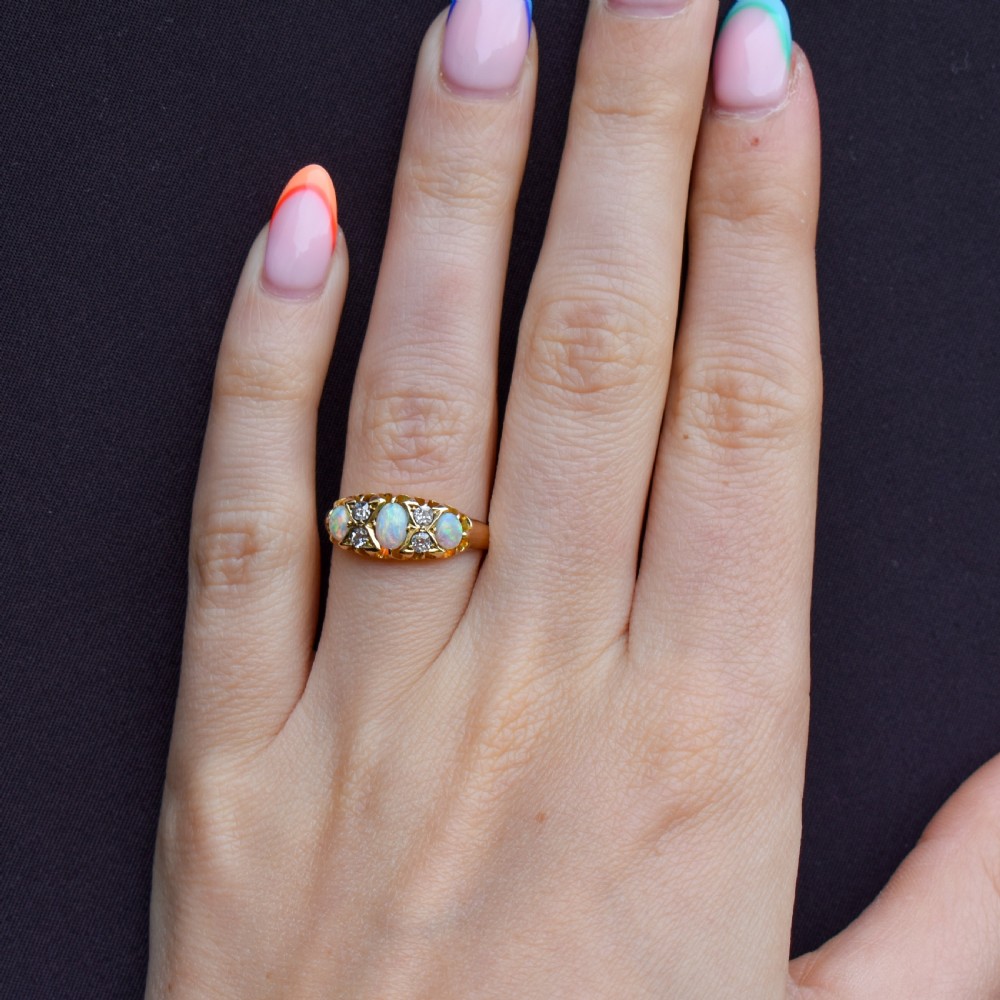 An antique 18ct yellow gold Edwardian boat ring set with three oval turquoise cabochons and four accent diamonds, featuring carved scrollwork along the gallery. View X