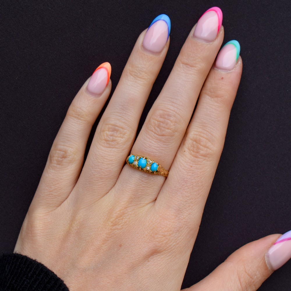 An antique 18ct yellow gold Edwardian boat ring set with three oval turquoise cabochons and four accent diamonds, featuring carved scrollwork along the gallery. View XII