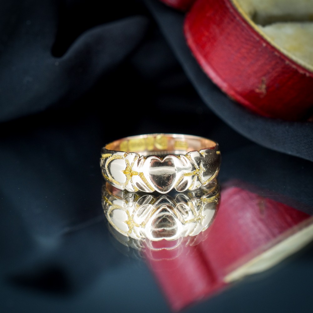 An antique Victorian 9ct yellow gold band ring featuring polished heart motifs set against textured background detailing. View IV