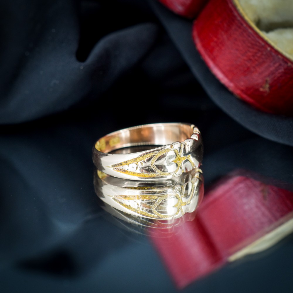 An antique Victorian 9ct yellow gold band ring featuring polished heart motifs set against textured background detailing. View V