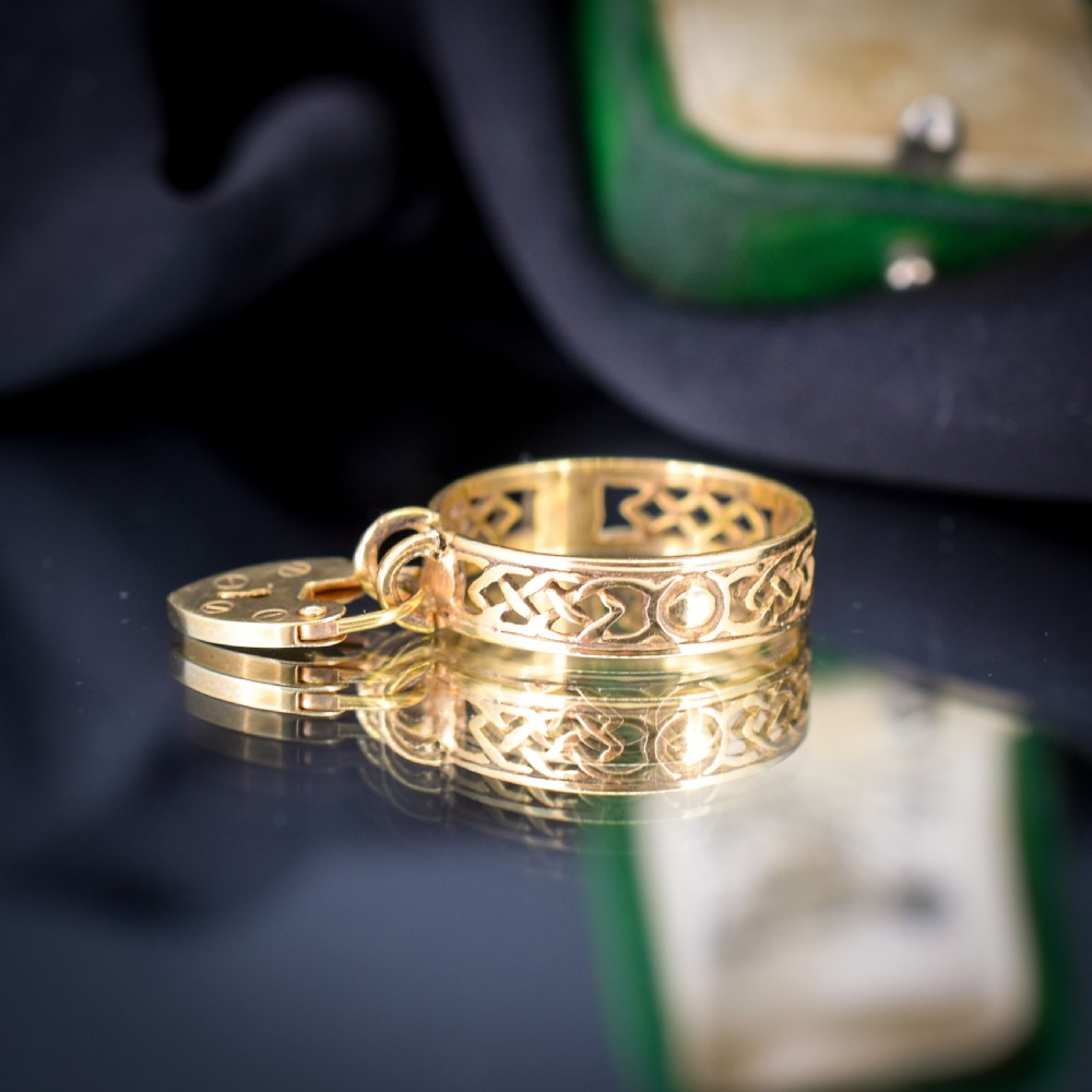 A 9ct yellow gold band ring featuring an openwork Celtic knot design with a suspended heart-shaped padlock charm at the front. View IV