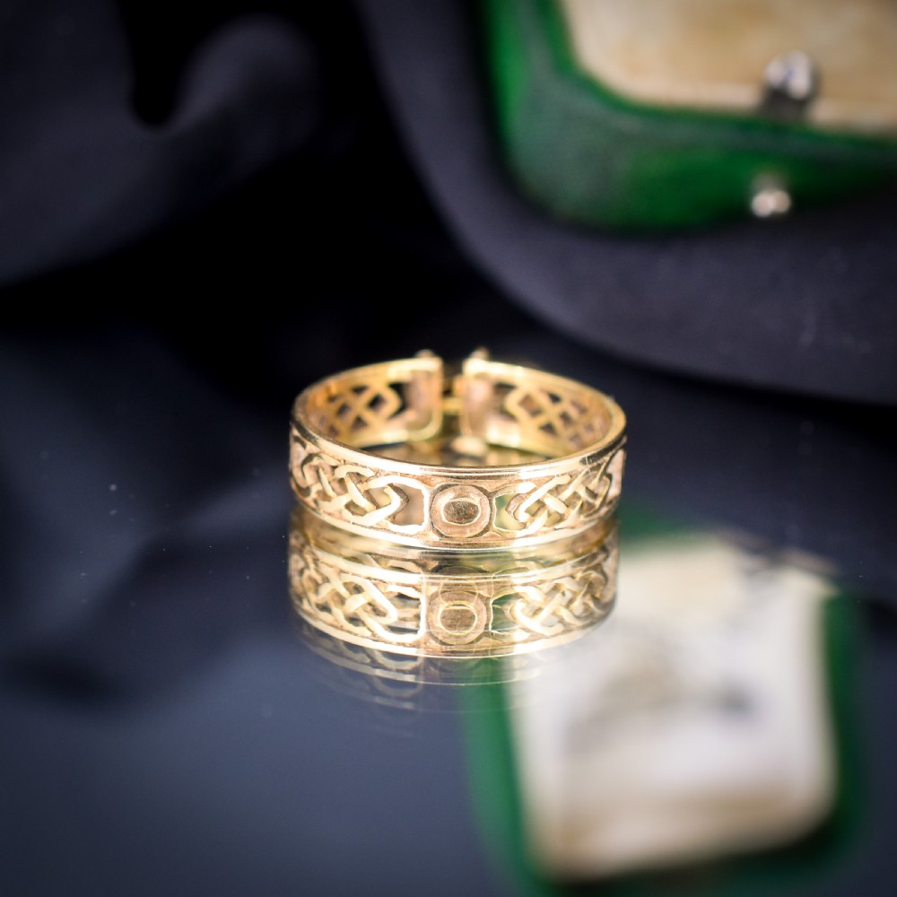 A 9ct yellow gold band ring featuring an openwork Celtic knot design with a suspended heart-shaped padlock charm at the front. View V