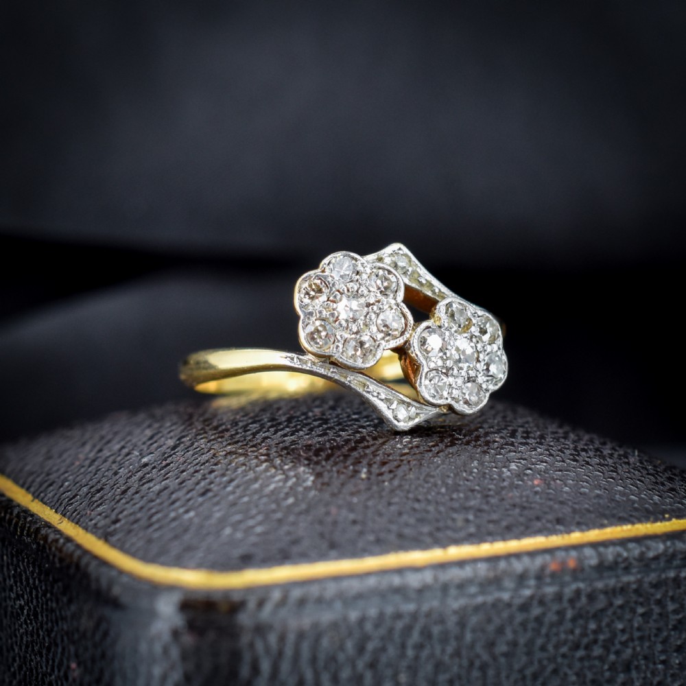 An antique 18ct yellow gold ring with a double twist band featuring two diamond-set flower clusters.