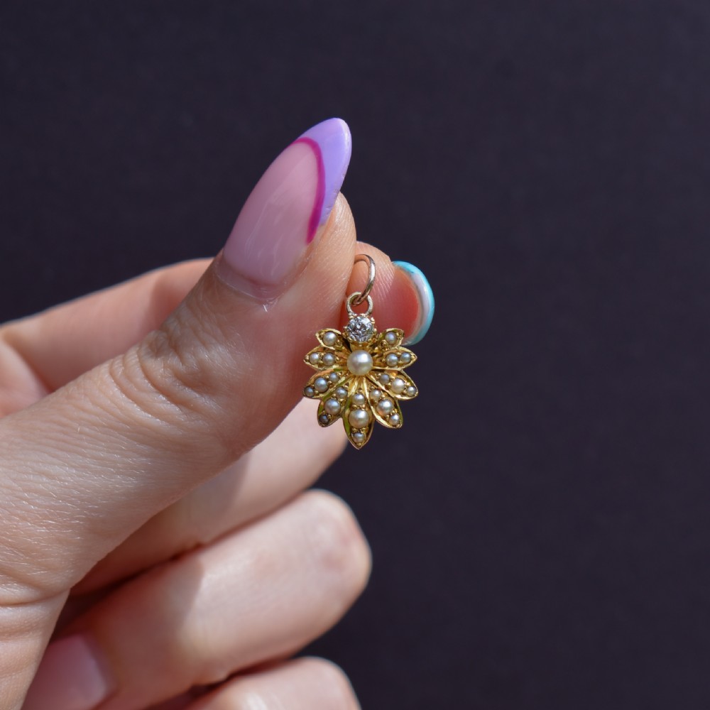 An antique floral gold pendant featuring a central pearl surrounded by seed pearl petals and topped with an old-cut diamond. View II