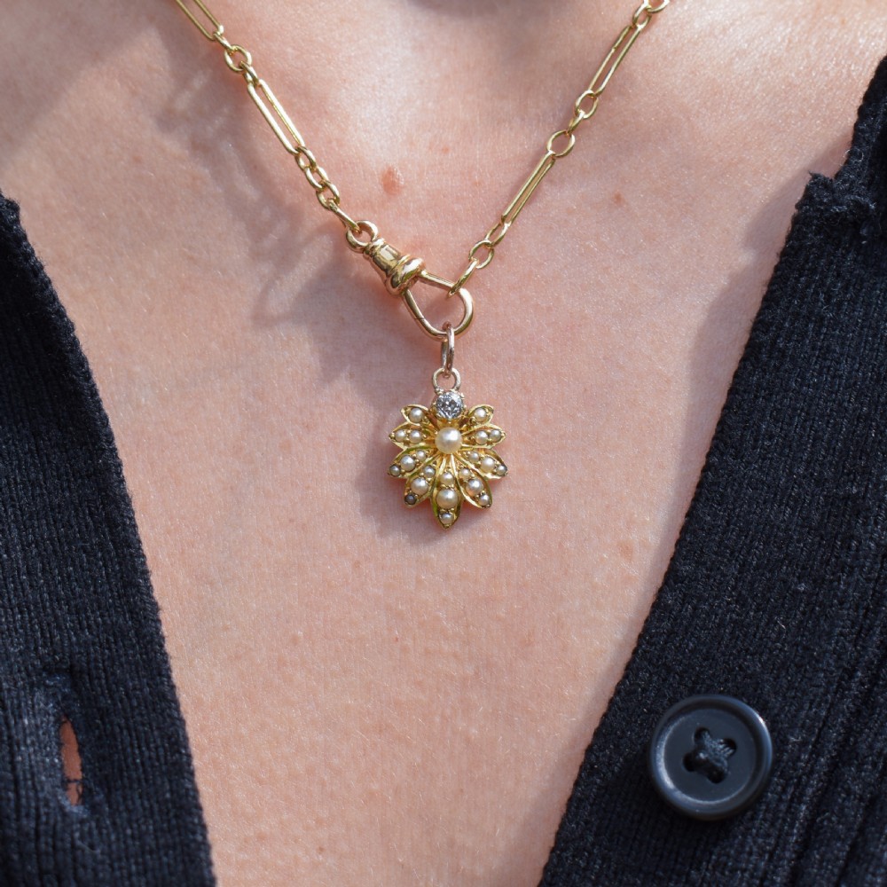 An antique floral gold pendant featuring a central pearl surrounded by seed pearl petals and topped with an old-cut diamond. View IV