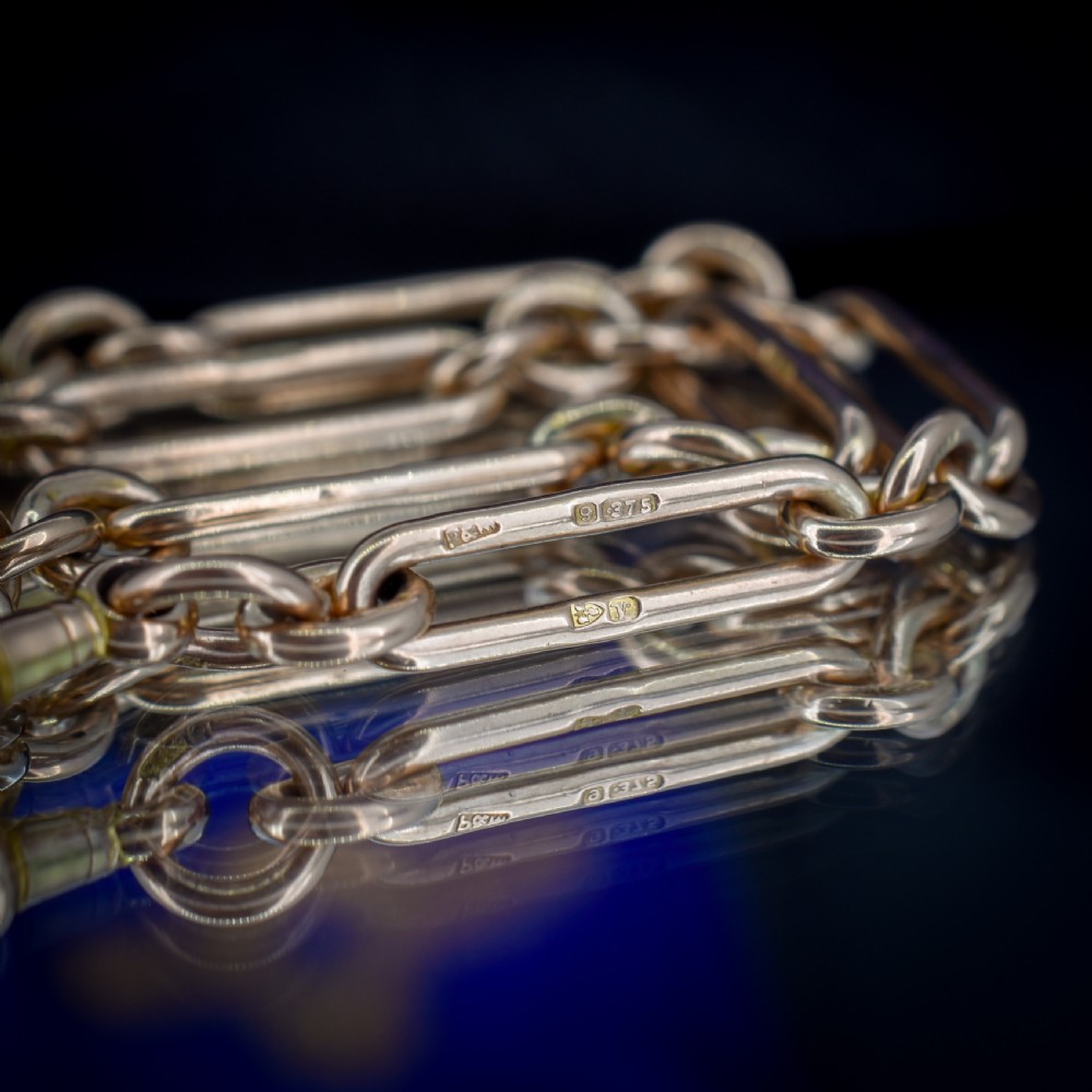An antique 9ct yellow gold Albert watch chain featuring elongated trombone links, connector rings, a T-bar, and a swivel clasp. View X