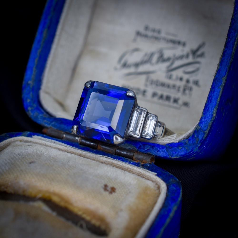 An Art Deco sterling silver cocktail ring set with a large square-cut blue gemstone and stepped baguette-cut side stones.