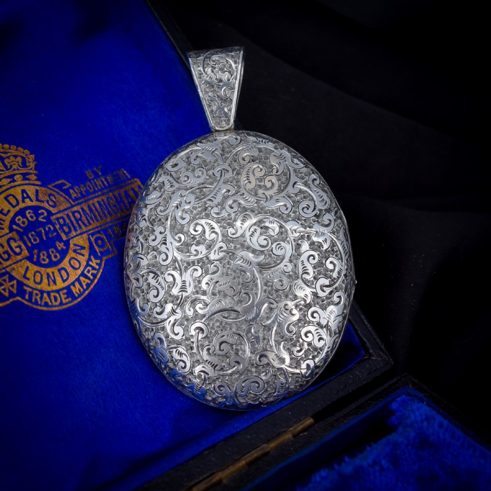 An oval sterling silver locket featuring elaborate hand-engraved scrollwork and a decorative foliage bail.