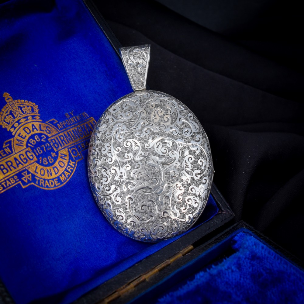 An oval sterling silver locket featuring elaborate hand-engraved scrollwork and a decorative foliage bail. View II