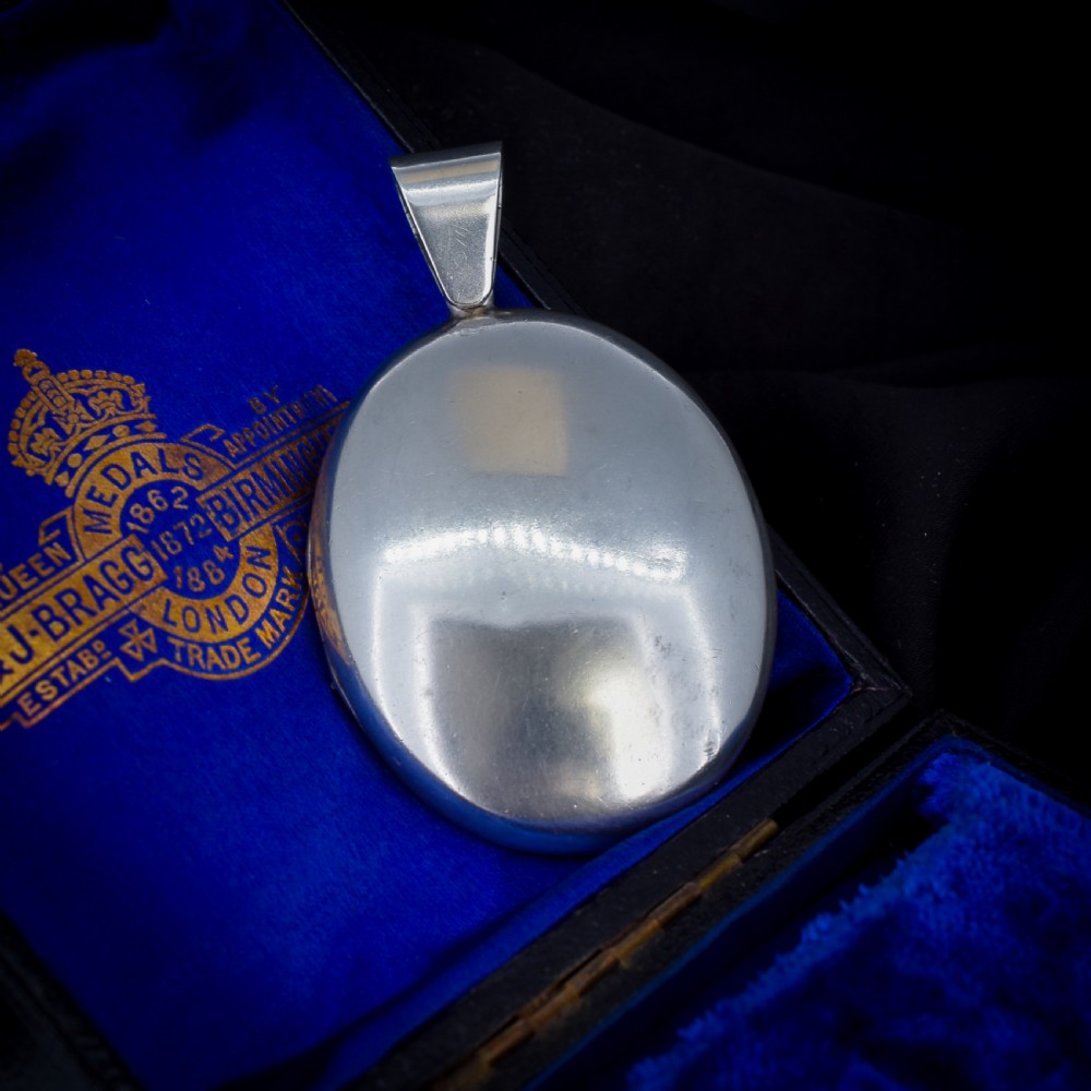 An oval sterling silver locket featuring elaborate hand-engraved scrollwork and a decorative foliage bail. View III