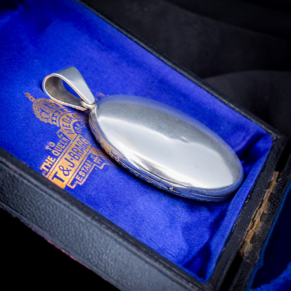 An oval sterling silver locket featuring elaborate hand-engraved scrollwork and a decorative foliage bail. View IV